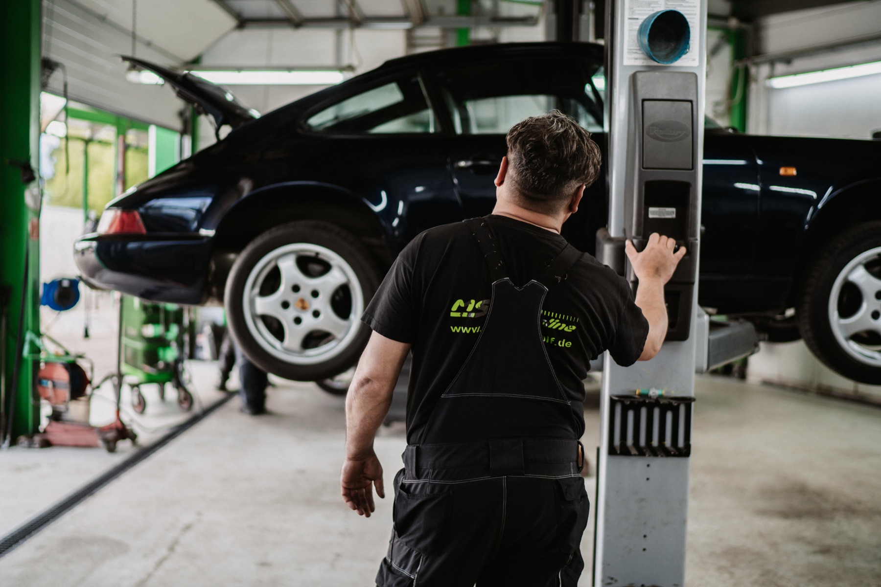 Werkstattmitarbeiter bedient die Hebebühne neben einem angehobenen Fahrzeug